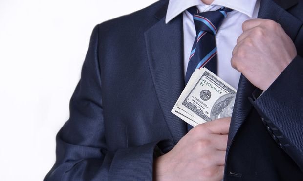 A man in a suit holding money and putting it into his jacket.