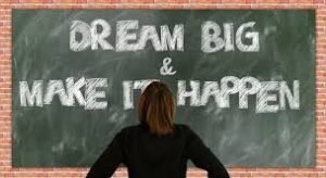 Lady looking at a chalk board that says "dream Big, and Make it happen"
