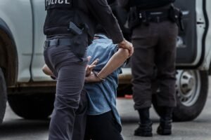 A guy handcuffed waiting to be loaded into the police car