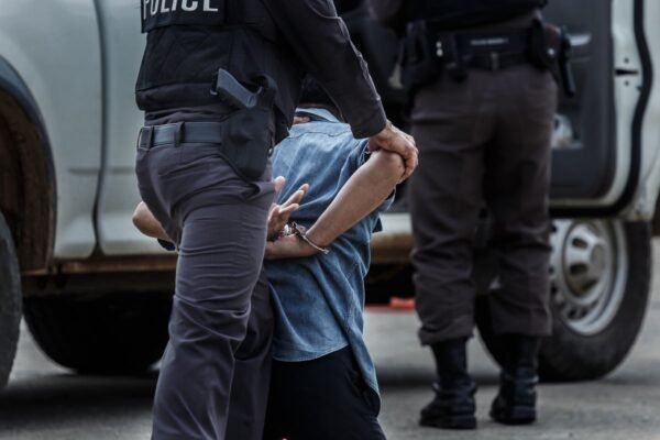 A guy handcuffed waiting to be loaded into the police car