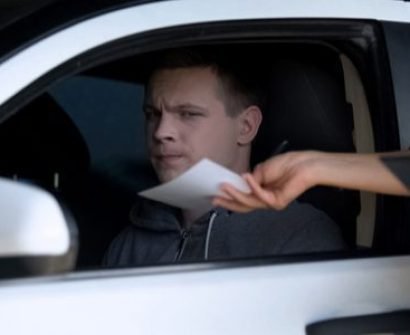 A person handing paper to another person in the back of a car.